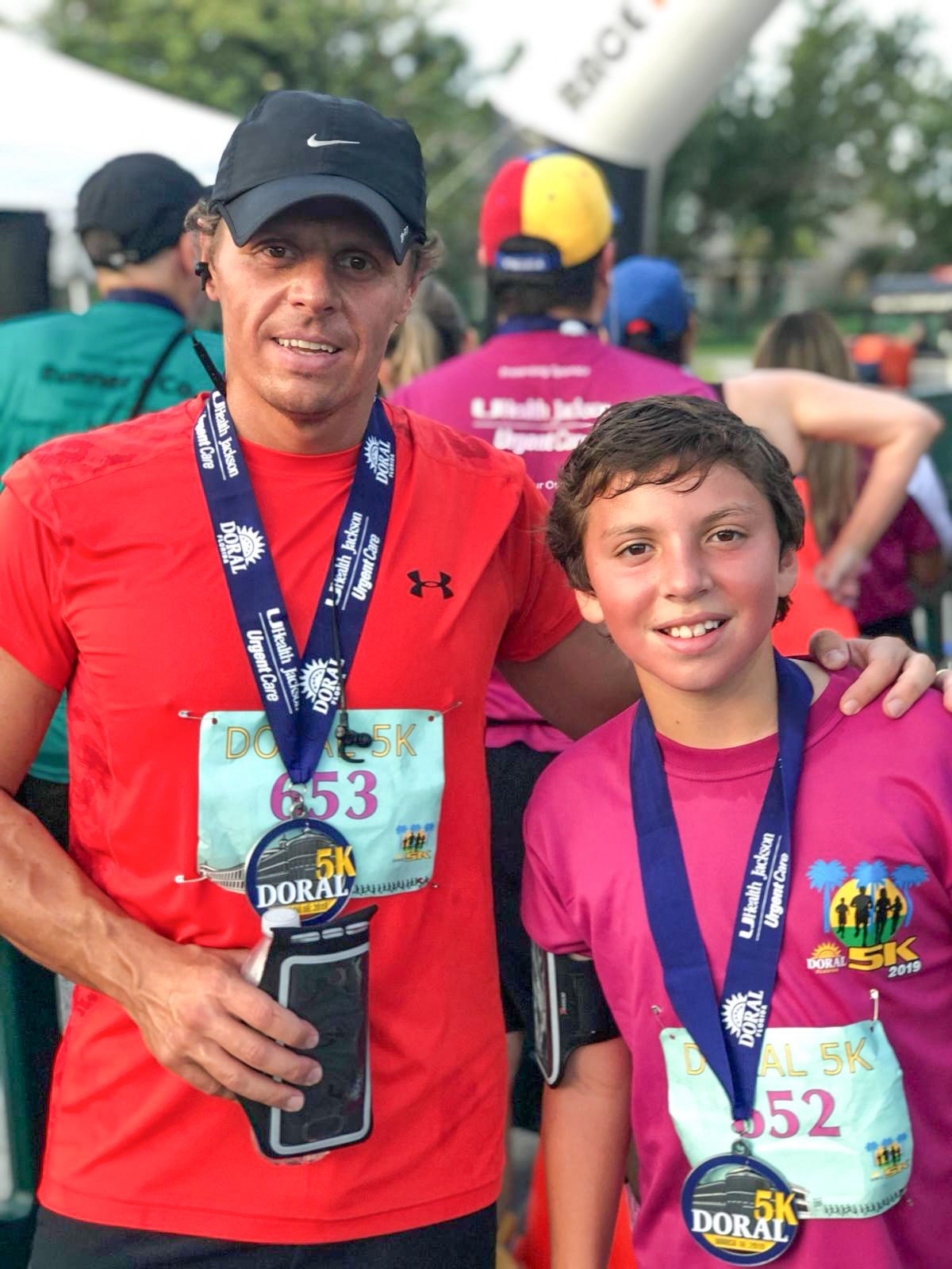 Two runners with race bibs and medals at a Doral 5K event.