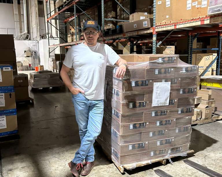 Fatly Good Founder standing next to a stack of boxes in a warehouse
