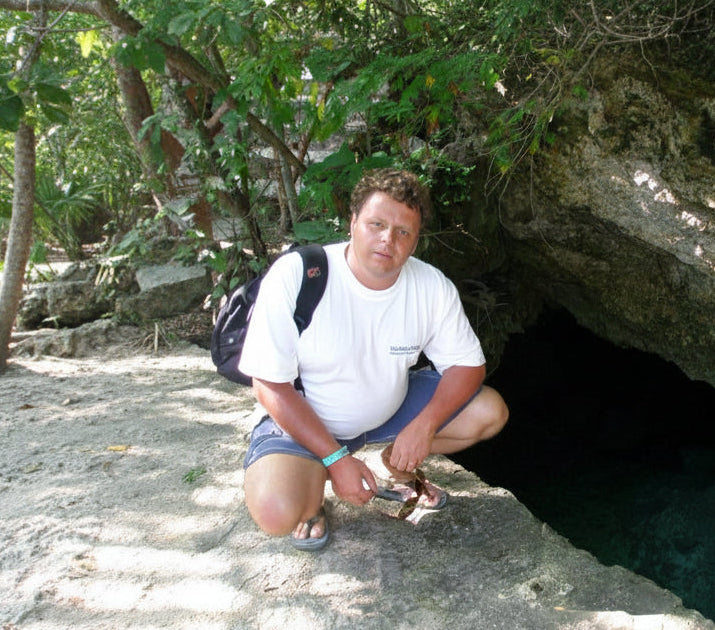 Man with a backpack crouching by a cave entrance in a natural setting